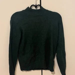 Mörkgrön stickad tröja från Vila - Mysig mörkgrön stickad tröja från Vila med ribbad hög hals och långa ärmar. Perfekt för kyligare dagar och enkel att matcha med olika outfits. Klassisk och stilren design.