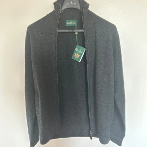 Alan Plaine fullzip  - Säljer en stilren grå tröja från Alan Plaine i 100% lammull. Tröjan har en hög krage med dragkedja och är perfekt för kyligare dagar. Den är både bekväm och elegant, vilket gör den till ett utmärkt val för höst och vinter. Skriv vid minsta fundering! Orginalpris: 2300