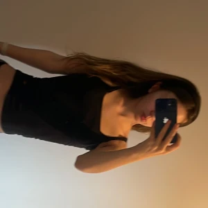 Svart croppad linnetopp - Säljer en enkel svart croppad linnetopp med smala axelband. Toppen är i stretchigt material och har en tight passform. Perfekt att styla med jeans eller kjol för en clean look. Köpte den ganska länge sen och råkade göra hål i tröjan.