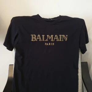 Svart t-shirt Balmain Paris - Säljer en svart t-shirt från Balmain Paris med gul broderad logga på bröstet. Klassisk rund hals och korta ärmar. Perfekt för dig som gillar stilrena och exklusiva plagg. Passar Storlek M-L, Priset kan diskuteras.
