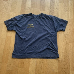 Mörkgrå t-shirt från donce de la sense - Mörkgrå t-shirt med rund hals och korta ärmar. På bröstet finns en liten gul text: 'D'ONCE DE LA SENSE'. Enkel och stilren design, perfekt för en avslappnad look.