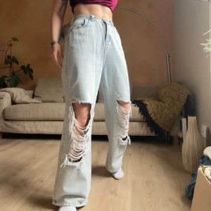 Ljusblå ripped jeans från The Kript - Säljer ett par ljusblå jeans från The Kript med stora slitningar på båda benen. Baggy med en tajt mellan hög midja. Väldigt sköna, nästan oanvända.