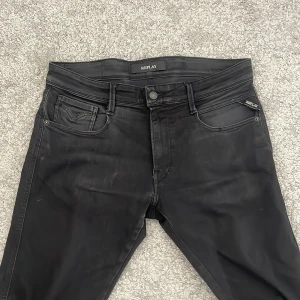 Svarta jeans från Replay - Säljer ett par svarta jeans från Replay med klassisk femficksdesign och diskret Replay-logga på bakfickan. Jeansen har normal passform och raka ben, perfekta till många olika outfits.