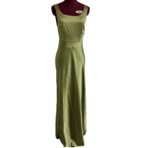 Ljusgrön långklänning med breda axelband och draperad rygg. Nypris: 1282kr - Säljer en elegant grön långklänning med breda axelband, fyrkantig ringning och draperad rygg. Klänningen har en smickrande passform och är tillverkad i ett mjukt, lätt och silk-aktigt material som faller snyggt längs kroppen. Klänningen hade ursprungligen en hög ringning men har  blivit omsydd av en sömmerska!Perfekt för en bal, ett bröllop eller en mer formell tillställning! Aldrig använd förutom testad förutom när den skulle sys om. 