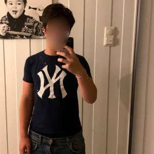 Mörkblå New York Yankees t-shirt - Säljer en mörkblå t-shirt med stor vit New York Yankees-logga på bröstet. Klassisk passform och rund halsringning. Perfekt för dig som gillar sportig stil eller är Yankees-fan.