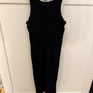 Svart ärmlös midklänning från 157 - Svart långklänning från 157 i 100% bomull. Klänningen är ärmlös med rund halsringning och har en enkel, stilren design som passar perfekt till sommaren. Går ungefär till knäna på mig, 170cm