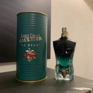 Jean Paul Gaultier Le Beau Le Parfum herrparfym - Jean Paul Gaultier Le Beau Le Parfum för herr, levereras i en grön metallcylinder med gulddetaljer. Flaskan har en unik design i form av en manlig torso i svart och grönblått glas med gulddetaljer. En lyxig och modern doft för honom.