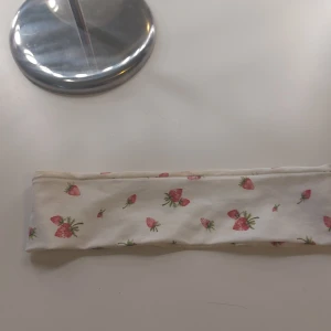 Hårband - Sött vitt diadem från H&M med små röda jordgubbar som mönster. Perfekt accessoar för att liva upp din look med en somrig känsla. Tillverkat i mjuk bomull för extra komfort.OBS.den har en fondation fläck som man kan se på första bilden 
