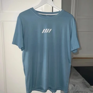 Ljusblå t-shirt med tryck - Inte mycket använd. Skulle säga att den är åt den relaxed fit hållet. Har 2 små noppror och ett pyttelitet hål på ryggen som inte syns tydligt. Axelbredd 46cm, längd 67cm.