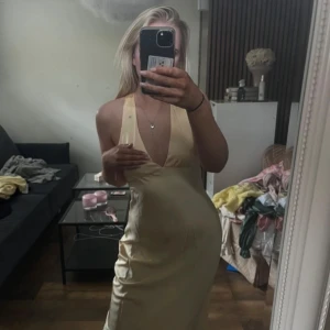 Champagnefärgad långklänning från Showpo - Säljer en elegant champagnefärgad långklänning från Showpo. Klänningen har djup v-ringning, breda axelband och öppen rygg med korsade band. Tillverkad i ett glansigt satinliknande material som ger en lyxig känsla.