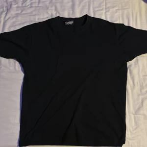 Svart t-shirt från Cover  - En klassisk svart t-shirt från Cover med rund halsringning och normal passform. Perfekt basplagg till garderoben. T-shirten är enkel och stilren utan tryck eller mönster.