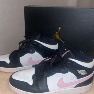 Nike Air Jordan 1 Mid  - Säljer ett par Nike Air Jordan 1 Mid med svart, vitt och rosa färgblock. Skorna har klassisk Jordan-logga på sidan och rosa swoosh samt detaljer på plösen. Perfekta för dig som vill sticka ut med en unik färgkombination. Aldrig kommit till användning.