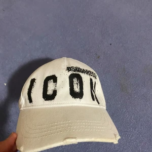 Vit keps från Dsquared2 med svart text - Vit keps från Dsquared2 med stor svart text 'ICON' broderad framtill och justerbar rem baktill. Kepsen har klassisk form med böjd skärm och ventilationshål.