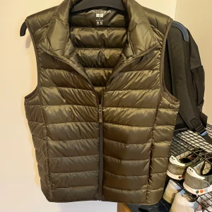 Olivgrön dunväst från Uniqlo - Säljer en olivgrön dunväst från Uniqlo Ultra Light Down. Västen har dragkedja framtill och är quiltad med en lätt och smidig känsla. Perfekt att bära som lager under jackan eller över en hoodie. Den är använd en gång helt ny