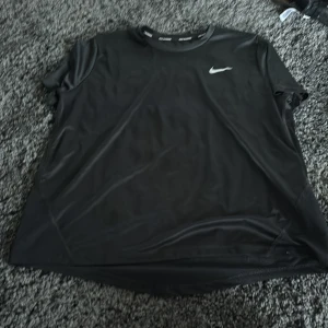 Svart Dri-Fit t-shirt från Nike - Säljer en svart Nike Dri-Fit t-shirt med rund hals och korta ärmar. Perfekt för löpning eller träning, tillverkad i ett lätt och snabbtorkande material. Diskret Nike-logga på bröstet och tryck på insidan av kragen.