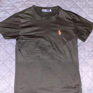 Svart t-shirt från Polo Ralph Lauren - Klassisk svart t-shirt från Polo Ralph Lauren med rund halsringning och liten röd broderad logga på bröstet. Perfekt basplagg med enkel och stilren design.