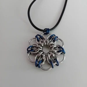Egentillverkad halsband  - Unikt halsband med en blommig berlock gjord av stålfärgade samt mörkblå matta metallringar. Hänger på ett svart snöre. Perfekt för dig som gillar handgjorda smycken med en cool design. Blomman är ca 3.5cm stort