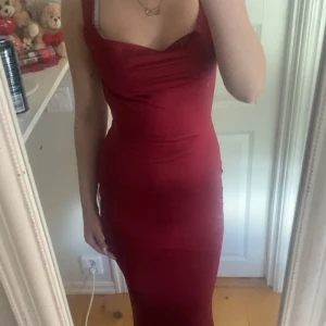 Vinröd långklänning med öppen rygg och rosett - Säljer en vinröd långklänning med tight passform. Klänningen har öppen rygg och en stor rosett baktill i midjan. Axelbandsmodell med draperad urringning framtill. Perfekt för festliga tillfällen.