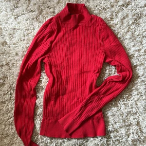Röd ribbad polotröja från New Yorker - Säljer en röd ribbad polotröja från New Yorker i storlek XS. Tröjan är stickad med lång ärm och har en hög polokrage. Perfekt för lager-på-lager och ger en snygg siluett. Snygg och enkel att matcha med jeans eller kjol.