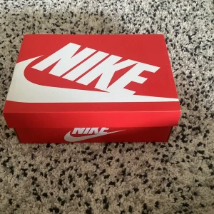 Nike Air Max 270 svart/vit - Säljer ett par Nike Air Max 270 i svart med vit sula och röda detaljer undertill. Skorna har en sportig design med synlig Air-enhet i hälen och diskret Nike-logga på sidan. Perfekta för dig som gillar streetwear och sneakers med modern look. 