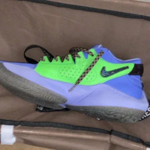 Nike sneakers i blått och grönt med mönstrad swoosh - Färgstarka Nike sneakers med blå och grön ovandel, svart och mönstrad swoosh samt flerfärgade skosnören. Skon har en robust platt sula och sportig design, perfekt för dig som gillar att sticka ut.