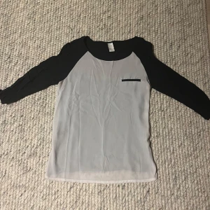 Svartvit blus med trekvartsärm från Vila - Säljer en snygg svartvit blus från Vila i storlek XS. Blusen har svarta trekvartsärmar och svart kant vid halsen, samt en liten dekorficka på bröstet. 