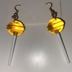 Örhängen med klubba-design i gult INGA PLUPPAR - Unika örhängen formade som gula klubbor med vita pinnar. Perfekt för dig som vill sticka ut med ett lekfullt och färgglatt smycke. Krokar i metallfärg och genomskinlig gul plast på klubborna.