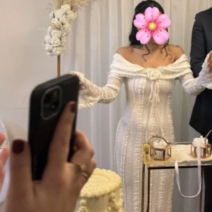 Vit långklänning med volang och spets - Romantisk vit långklänning med offshoulder och långa ärmar. Klänningen har vackra volangdetaljer och spets längs hela plagget samt knyt framtill. Perfekt för speciella tillfällen. Använd endast i 2 timmar på min Nikkah. 