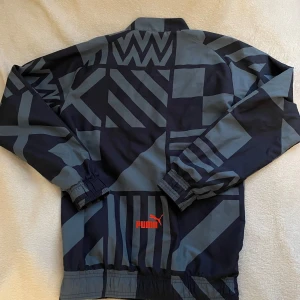 Mörkblå vindjacka från Puma x Marseille - Säljer en snygg vindjacka från Puma X Marseille. Jackan har ett grafiskt mönster i mörkblått och grått, som inte många har. Storlek XS