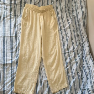 Beige linnebyxor från RYVLS - Säljer ett par ljusbeige linnebyxor från RYVLS med resår i midjan och raka ben. Byxorna har två sidofickor och är tillverkade i ett svalt och luftigt linnematerial, perfekta för varma dagar. På bild 4 ser vi även en liten defekt, den syns knappt men ändå bra att veta. Skriv privat för funderingar och frågor😁