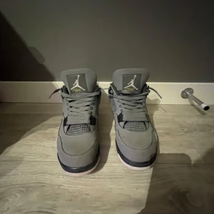 Gråa Air Jordan 4 sneakers - Säljer ett par gråa Air Jordan 4 sneakers med vita och svarta detaljer samt gula inslag på sulan. Skorna har snörning, meshpaneler på sidorna och den klassiska Jumpman-loggan på baksidan och tungan. Perfekta för dig som gillar streetwear. Skick 8/10 då dom endast är andvända 6-8 gånger. Lite smutsiga men tvättar innan jag skickar! Pris kan diskuteras! De är bara att höra av sig vid frågor!🫡