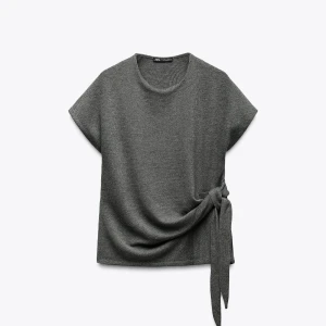 Grå topp med knytband i sidan - Snygg grå topp med rund halsringning och korta ärmar. Perfekt att styla med både jeans och kjol.