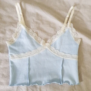 Ljusblå ribbad linnetopp  - Supersöt ljusblå ribbad linnetopp från H&M Divided med smala justerbara axelband och vit spetskant längs urringningen och under bysten. Croppad modell och är i storlek XS men skulle säga att det också passar XXS och S. Den är perfekt för sommaren och varma dagar. Sömmen vid ena axelbandet har lossnat, som man kan se på sista bilden, men sitter fortfarande kvar och syns inte så mycket. Säljer då den inte kommer till användning!