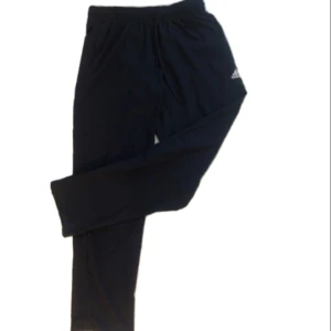 Mörkblå luftiga träningsbyxor från Adidas - Mörkblå luftiga träningsbyxor från Adidas med dragsko i midjan och diskret logga på låret. Byxorna har en avslappnad passform och är perfekta för chill eller träning. Tillverkade i mjukt material som känns skönt mot huden.