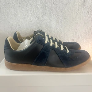 Maison Margiela GATS navy blue - Maison margiela GATS i navy med ovandel i både mocka och skinn, vita snören och klassisk gummisula i beige. Skorna har en stilren och tidlös design med rund tå och kontrasterande material. Perfekta för dig som gillar en clean och sportig look.