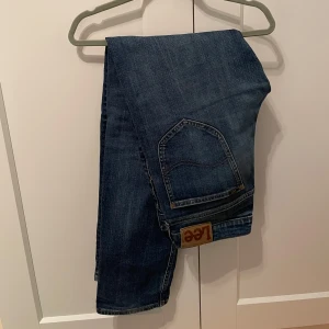 MörkBlå jeans från Lee - Snygga blå jeans från Lee i modellen Daren Zip Fly. De har en klassisk femficksdesign och en dragkedja. Perfekta för en avslappnad stil. I nyskick! Nypris ligger på 1300kr, bara att höra av sig vid frågor! Har även ett par exakt likadana i samma storlek fast i en ljusare blå ute om man vill köpa båda tillsammans för ett mycket bra pris!
