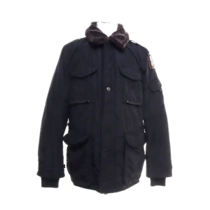 Svart vinterjacka från Parajumpers - Säljer en svart vinterjacka från Parajumpers med pälsimitation på kragen och flera stora fickor framtill. Jackan har lång ärm, dragkedja och knappar samt patch på ena ärmen. Perfekt för kalla dagar. 