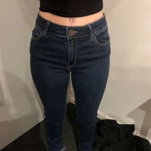 Mörkblå skinny jeans - Säljer ett par mörkblå skinny jeans med hög midja och klassiska fem fickor. Jeansen har en smal passform och stängs med dragkedja och knapp framtill. Perfekta till vardags och lätta att matcha med olika toppar.