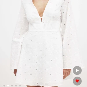 Vit kortklänning med öppen rygg  - Superfin vit kortklänning med v-ringning, lång ärm och öppen rygg. Klänningen har broderade blommor i tyget och markerad midja. Perfekt till studenten! Den är aldrig använd endast testad 