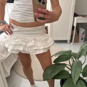 Lågmidjad Vit volangkjol från Zara - Supersöt vit kortkjol från Zara med flera lager volanger. Kjolen har en tight passform upptill. Använd 2 gånger förra sommaren men är tyvär för liten nu😢Passar perfekt till sommarens alla outfits! Inbyggda shorts vilket är superskönt!! 
