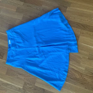 Blå omlottkjol med dragkedja - Säljer en blå omlottkjol med asymmetrisk nederkant och dragkedja i sidan. Kjolen har en stilren look och är tillverkad i ett mjukt, lätt material som ger ett snyggt fall. Perfekt för dig som vill ha en enkel men trendig kjol. Smutsig vid dragkedjan på baksidan, har inte försökt få bort. Tyvärr för liten för mig. 