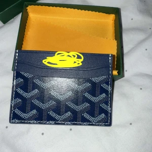 Blå korthållare  - Säljer en stilren blå korthållare med en klassisk mönster i vitt och grått. Korthållaren har flera fack för kort och en gul insida. Perfekt accessoar för dig som vill ha något både snyggt och praktiskt.