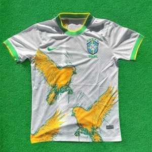 Vit Brasilien fotbollströja med papegoja-tryck - Säljer en vit Brasilien fotbollströja från Nike med gröna och gula detaljer. Tröjan har korta ärmar, grönt och gult runt kragen och ärmsluten samt ett stort papegoja-tryck framtill. Brasilien-emblem och Nike-logga på bröstet.