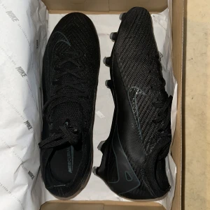 Svart Nike Air Zoom Mercurial Vapor 16 Elite AG-PRO - Säljer ett par svarta konstgräs skor eftersom dom är för stora(storlek 43). Skorna har använts 2 träningar.    Medföljer:Fotbollskor, påsen och boxen