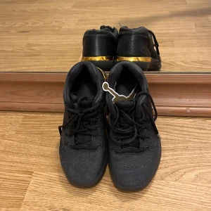 Svarta sneakers med gulddetalj / Jordan skor  - Säljer ett par svarta sneakers med snygg guldfärgad detalj på hälen. Skorna har snörning och en rund tå, ovandelen är i textil och syntet. Perfekta för dig som vill ha en stilren och sportig look.