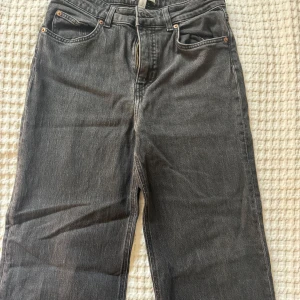 Svarta raka jeans från H&M - Säljer ett par svarta jeans från H&M med klassisk femficksdesign och raka ben. Jeansen har normal passform, dragkedja och knapp framtill samt bälteshällor. Perfekta till många olika stilar.