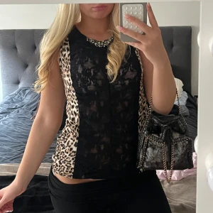 Svart spetsblus med leopardmönster - Snygg festtopp med svart spets framtill och leopardmönster på sidorna och baktill. Rund halsringning med stenar. 