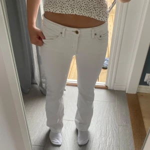 Vita bootcut jeans med strassdetalj - Snygga vita jeans med bootcut passform och låg midja. Jeansen har klassiska fem fickor och en cool strassdetalj på bakfickan. Tillverkade i stretchig bomullsblandning för skön passform. Perfekta för dig som vill ha en fräsch och stilren look.