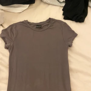 Mörkbrun tajt t-shirt Gina Tricot - En basic mörkbrun t-shirt från Gina Tricot i tight passform. Modellen är kortärmad med rund halsringning och tillverkad i mjuk bomull. Perfekt att styla med jeans eller kjol för en clean look.