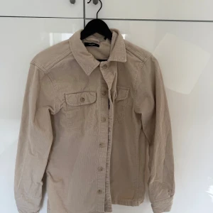 Beige manchester-skjorta från Jack&Jones - Säljer en beige skjorta i mjuk manchester från jack&Jones. Skjortan har klassisk krage, knäppning framtill och två bröstfickor med lock. Perfekt för dig som gillar en avslappnad men stilren look.